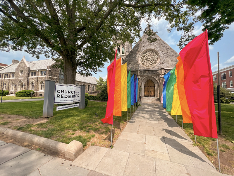 The Church of Redeemer with its sign and colorful flags out front on a clear sunny day.